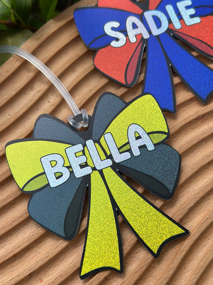 Personalized glitter holographic cheer bow bag tag with name Bella in yellow and black, custom team cheer gift by Olive + Rae